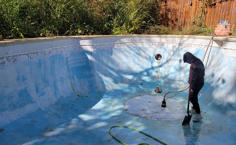 Person cleaning an empty swimming pool with a shovel.