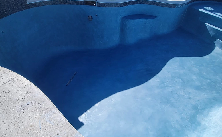 Empty inground swimming pool with light blue surface and curved edges.