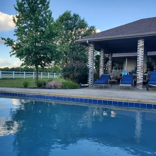 Outdoor poolside patio with lounge chairs and brick columns near lush greenery.