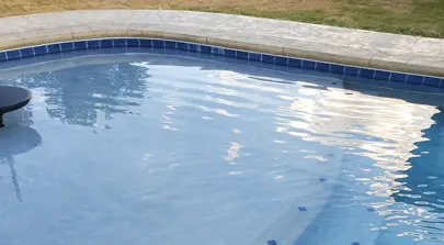 Curved swimming pool edge with tiled border and water reflections.