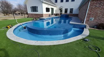 Backyard inground pool next to a large house with grassy lawn.
