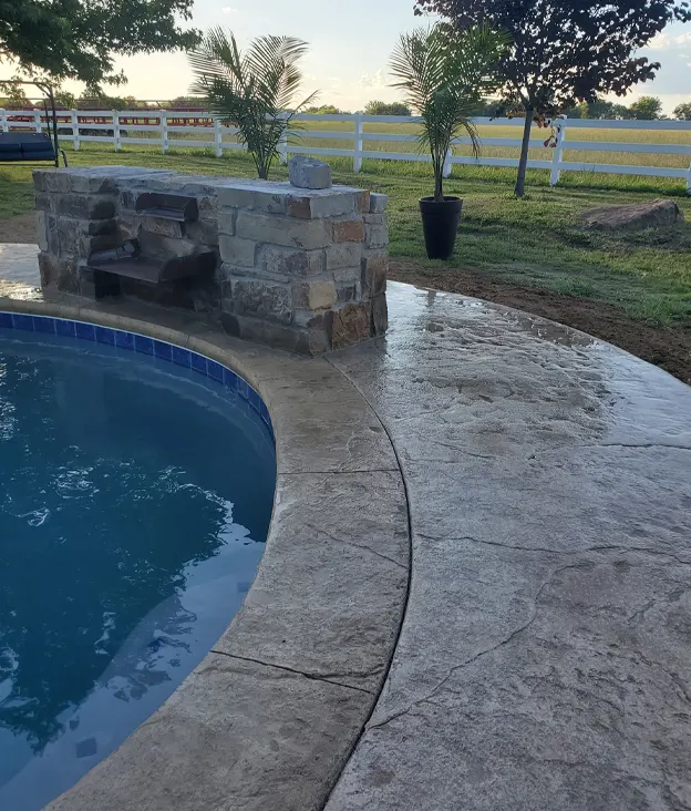Curved stone poolside with brick wall and potted plants in the background.