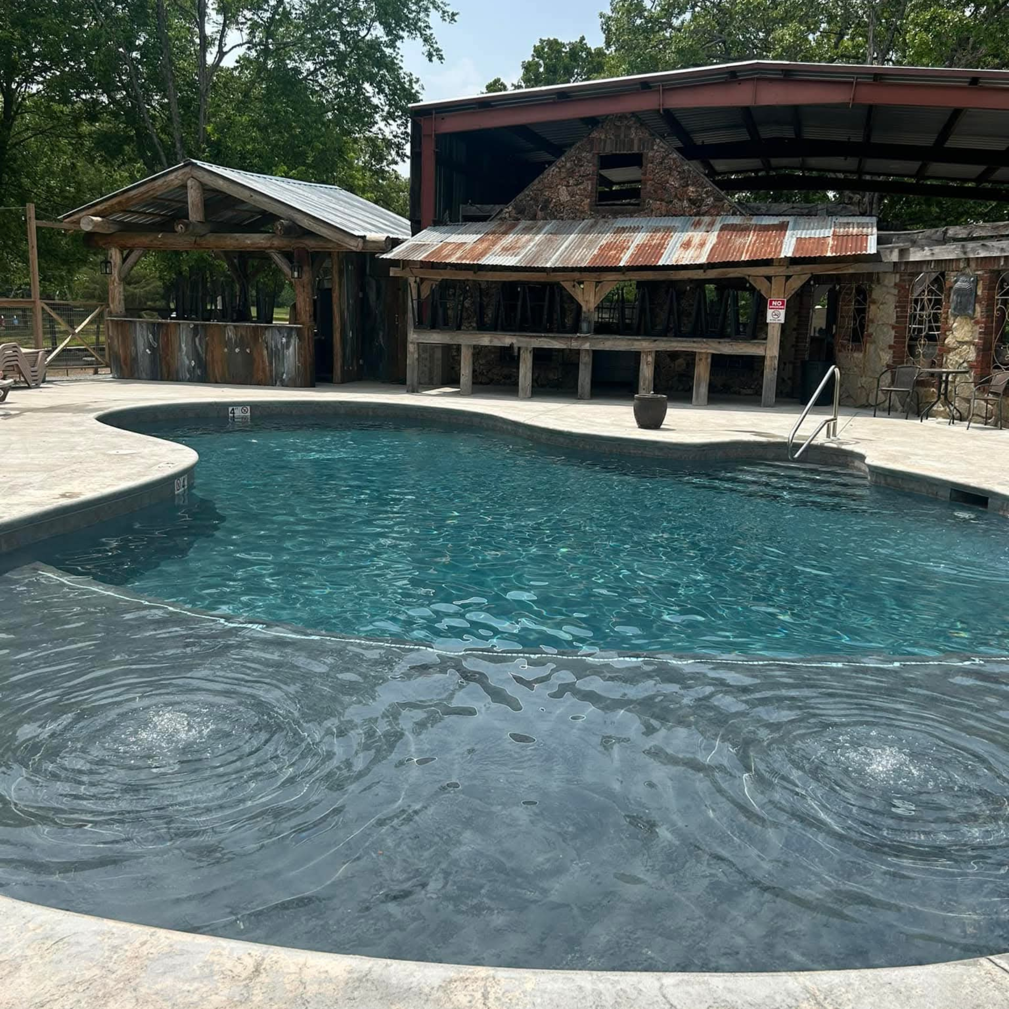 Outdoor swimming pool with rustic wooden and stone buildings in the background.
