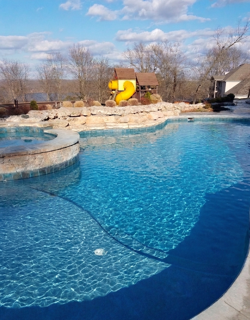 Clear blue swimming pool with rock waterfall and yellow slide.